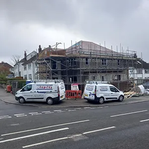 A couple of vans parked in front of a building under construction.