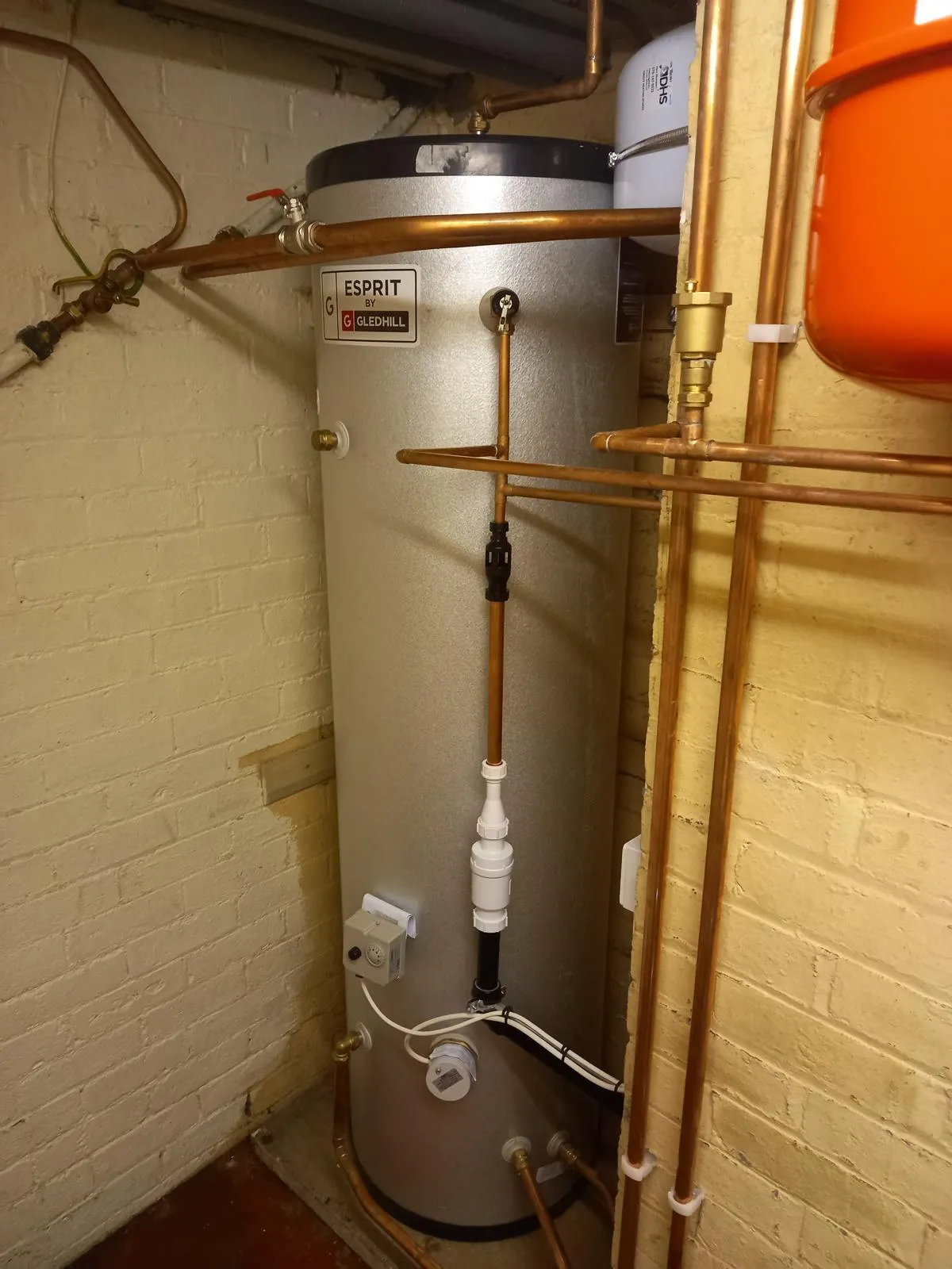 A water heater in a room with exposed pipes.